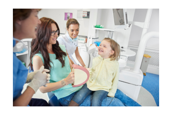 Child, parent, and dental hygienists laughing. Child appears comfortable and happy. 